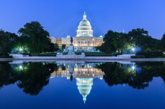 Night photo of the Capitol of the United States with a reflection in the pool in front.